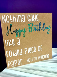 brown Kraft paper card stock background with text that reads "nothing says Happy Birthday like a folded piece of paper -you're welcome" in complimentary white and holographic blue/green colours 