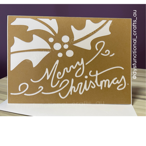 On a base of white card stock sits a layer of brown kraft paper, it has holly leaves and "Merry Christmas" cut out in a script handwritten like font which reveals the white card stock below